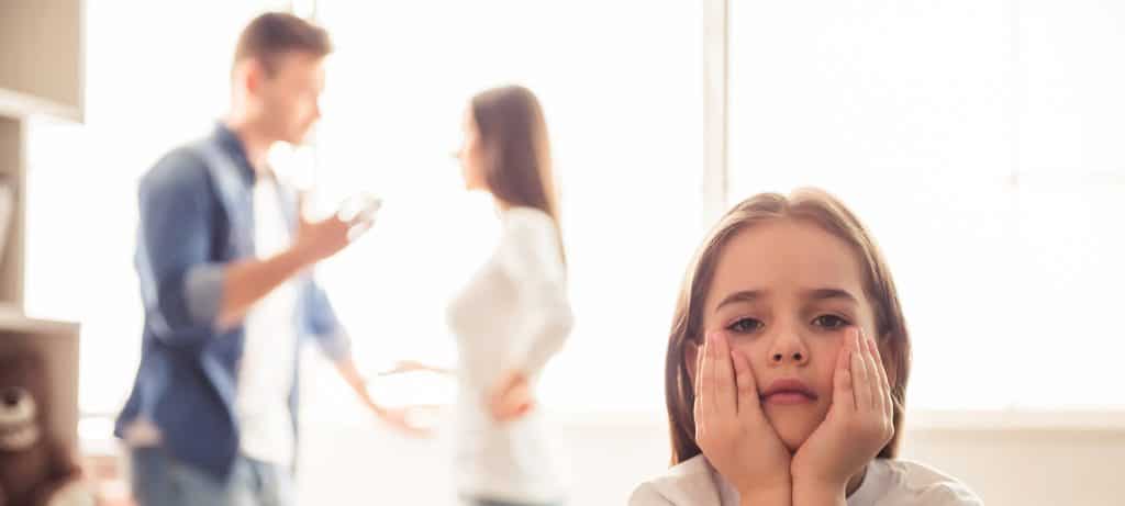 Girl looks sad as parents argue in the background