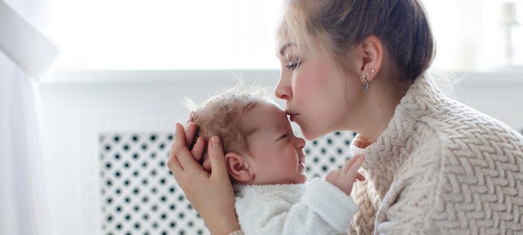 Woman holds her newborn baby and kisses it on forehead